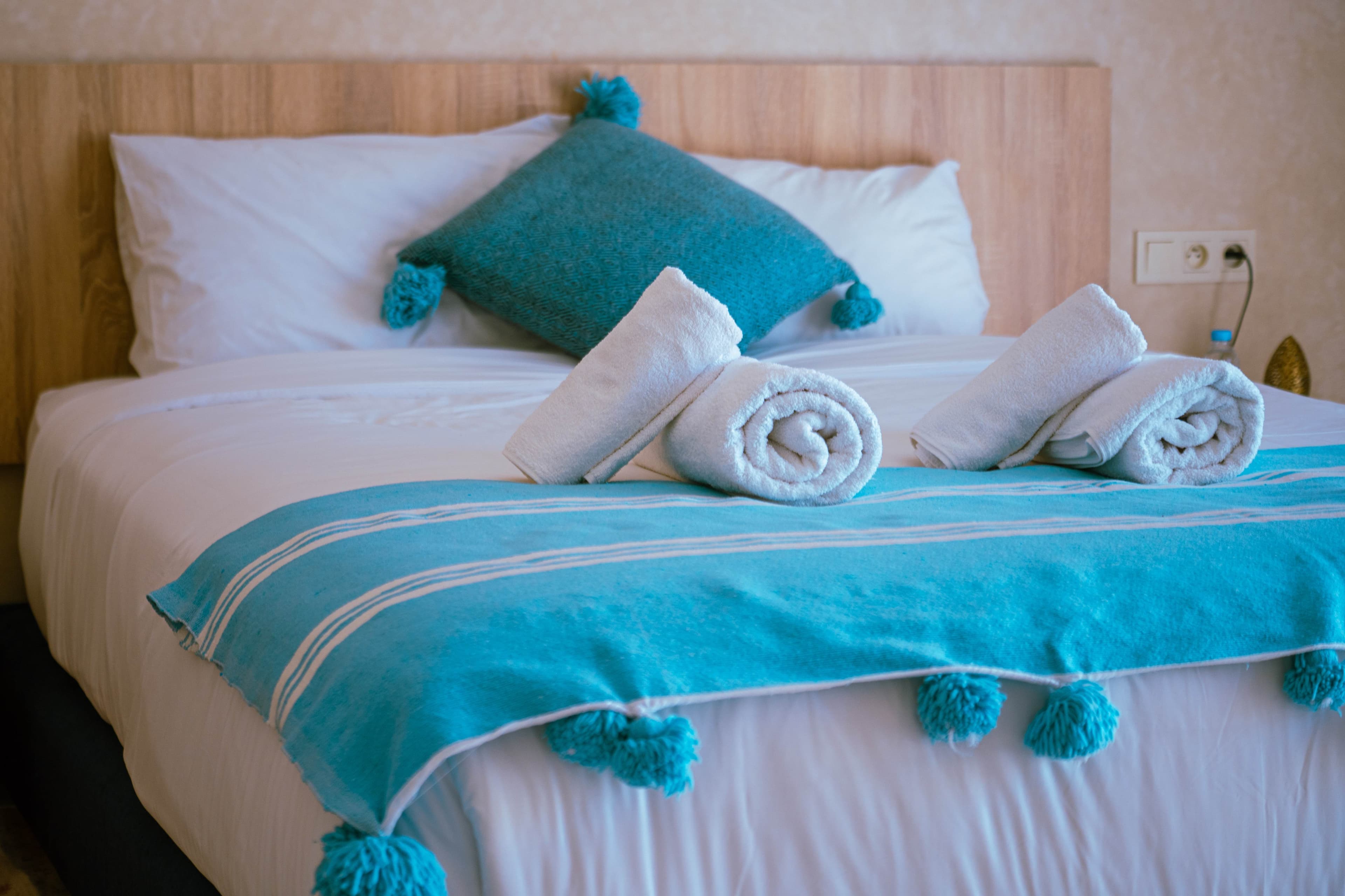 Close-up of bed with teal throw and rolled towels